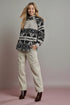 Woman wearing a patterned sweater and beige pants against a plain background