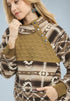Woman wearing a patterned sweater with a quilted brown bib over the chest against a light blue background.