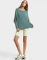 Woman wearing a green oversized top and white shorts on a light gray background