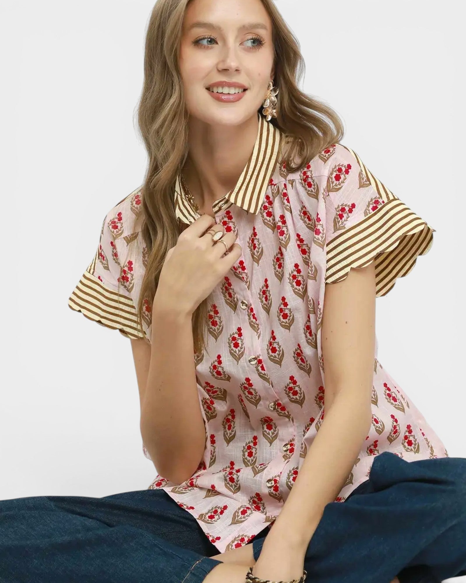Woman wearing a patterned blouse with short sleeves and a collar, sitting against a plain background.