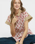 Woman wearing a patterned blouse with short sleeves and a collar, sitting against a plain background.