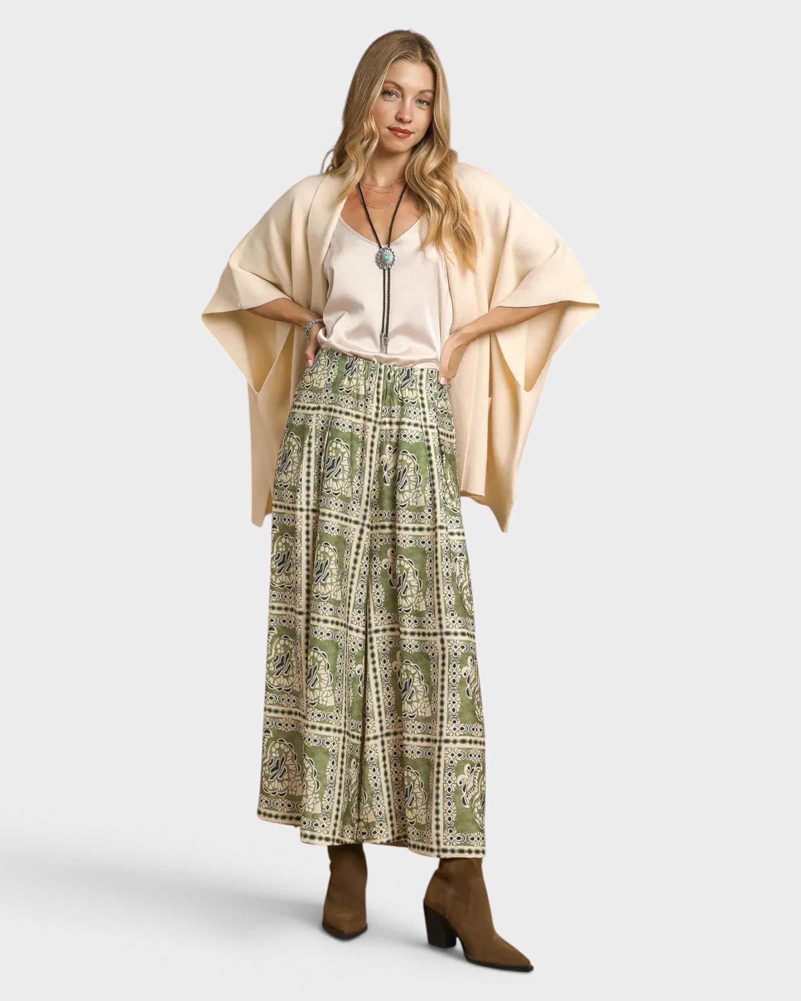 Woman wearing a beige cardigan, white top, and green patterned skirt on a white background