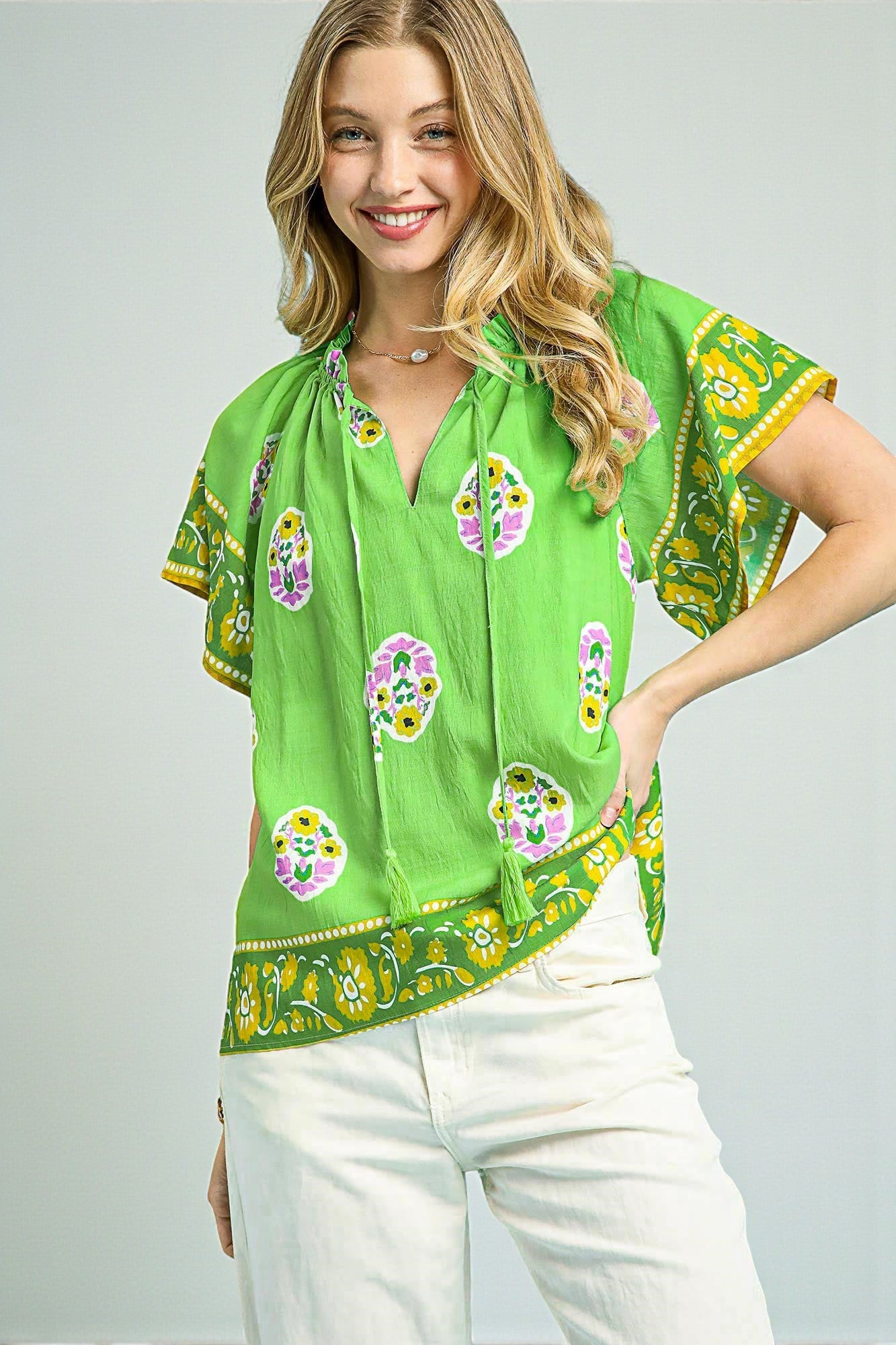Woman wearing a green patterned blouse with white pants on a gray background