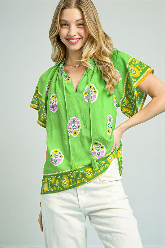 Woman wearing a green patterned blouse with white pants on a gray background
