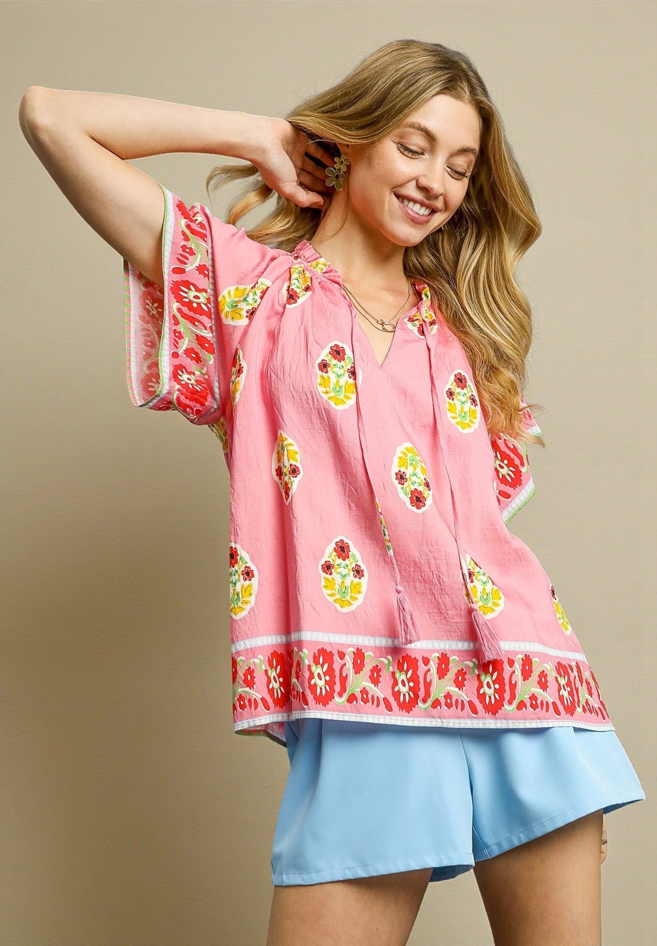 Woman wearing a pink floral top and blue shorts against a beige background