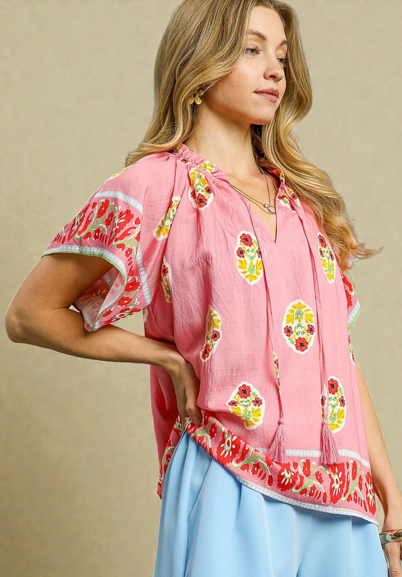 Woman wearing a pink floral blouse with blue pants against a beige background