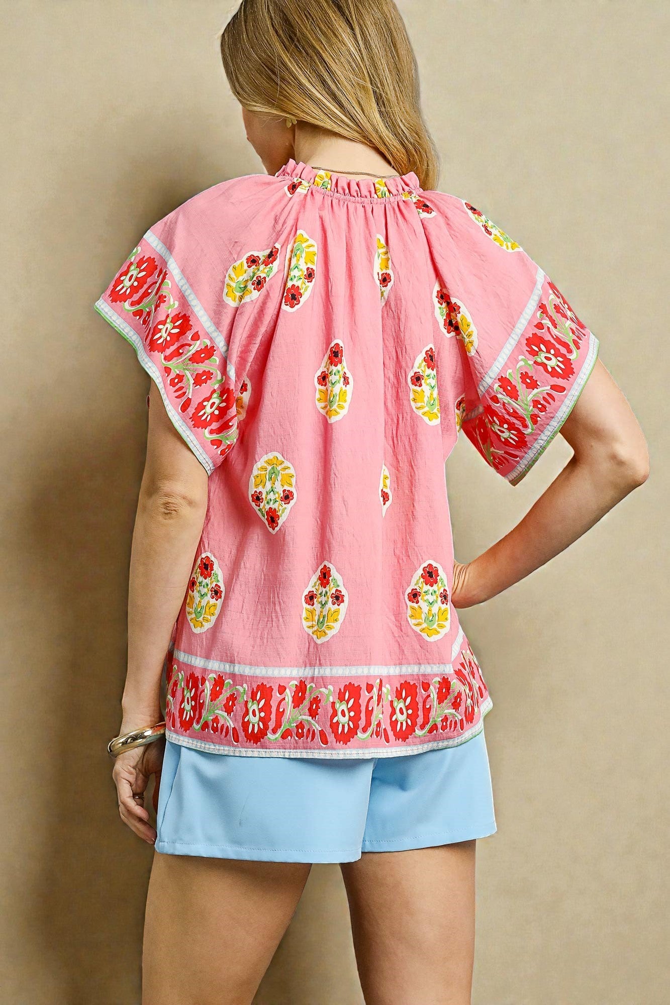 Woman wearing a pink embroidered top with floral patterns and light blue shorts against a beige background