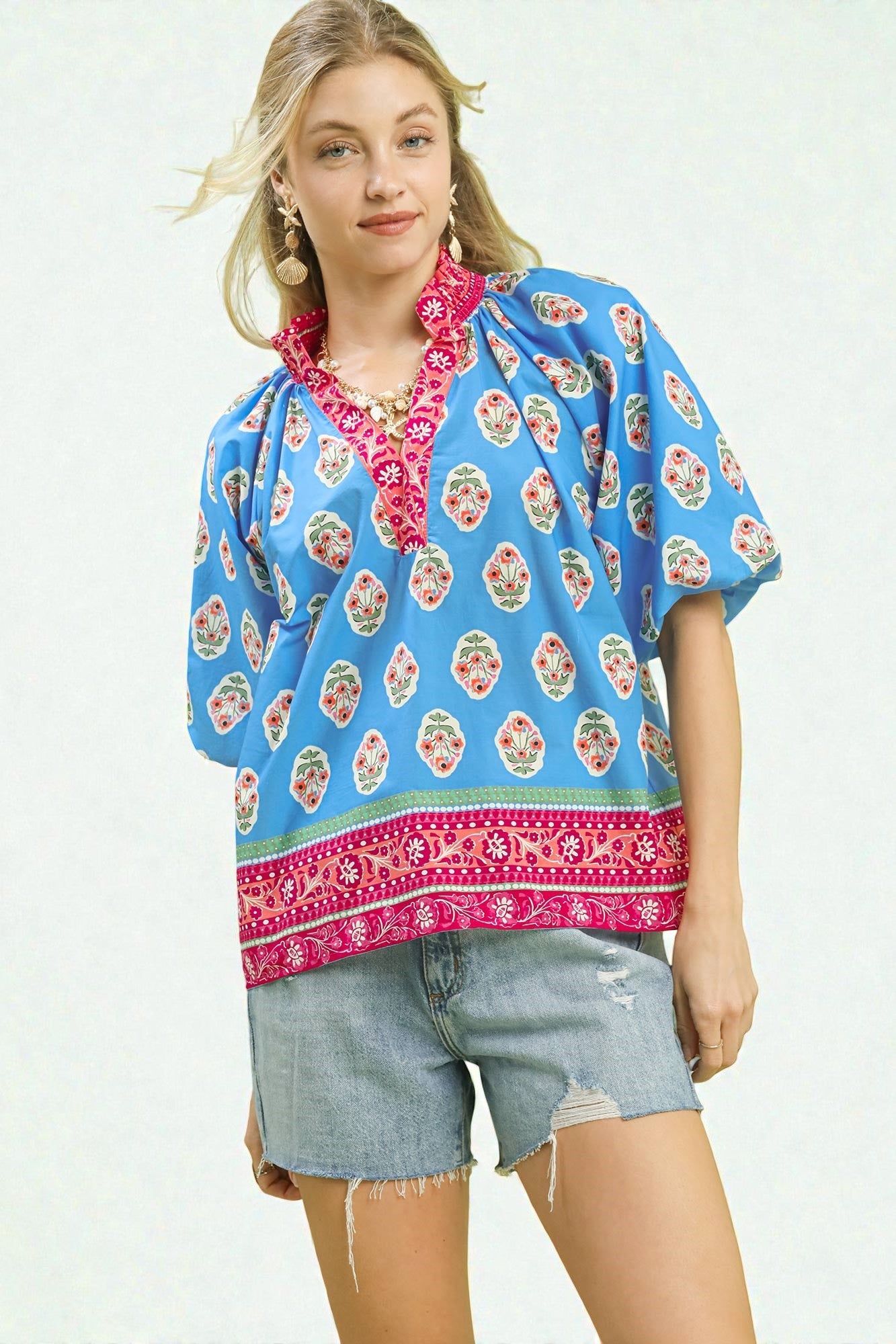 Woman wearing a blue floral patterned top with pink trim on a white background