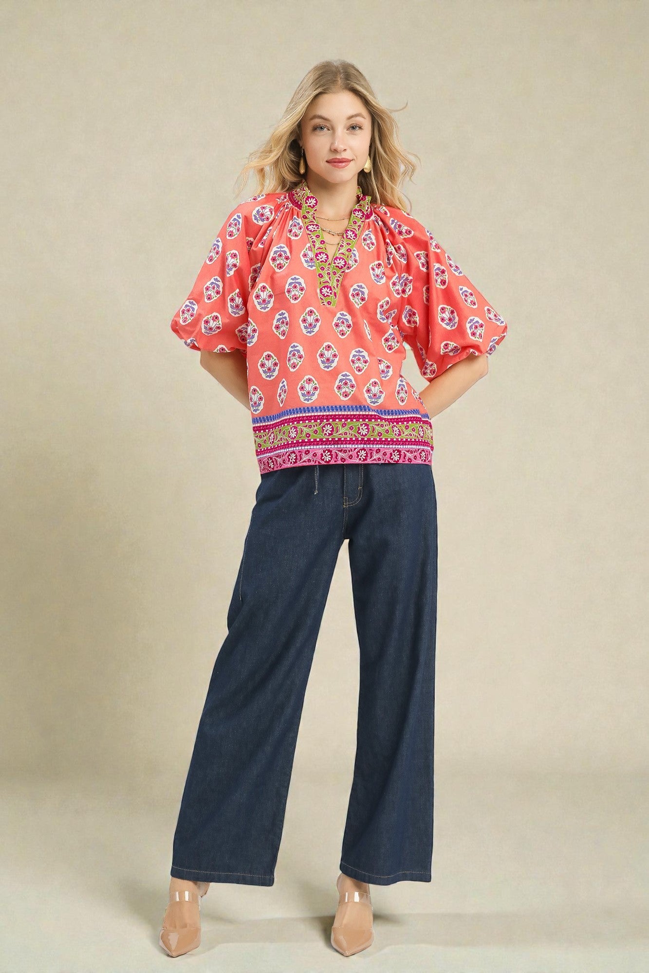 Woman wearing a pink patterned blouse and blue jeans against a beige background