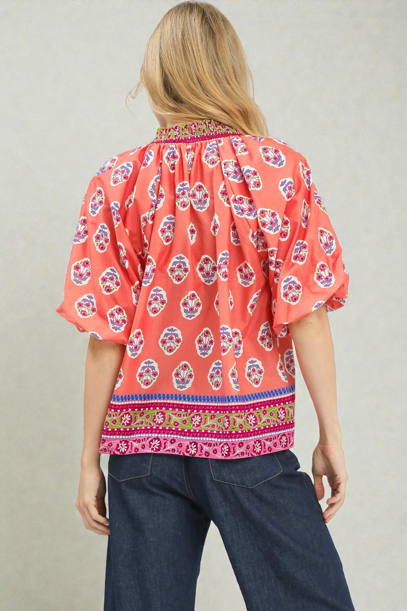 Woman wearing a red patterned blouse with blue pants on a plain background