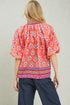 Woman wearing a red patterned blouse with blue pants on a plain background