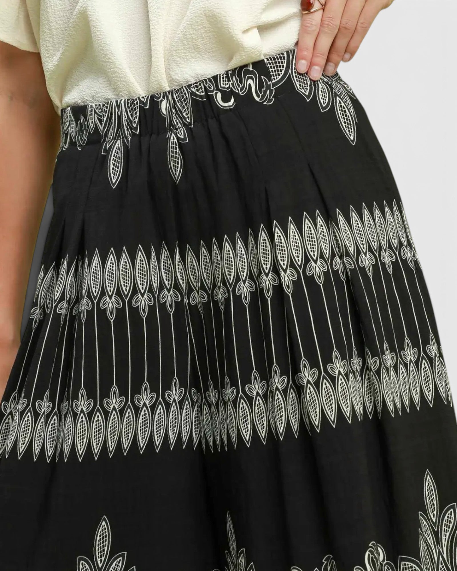 Black wide-leg pleated skirt with white embroidered leaf and vine patterns, shown on a model wearing a cream top.