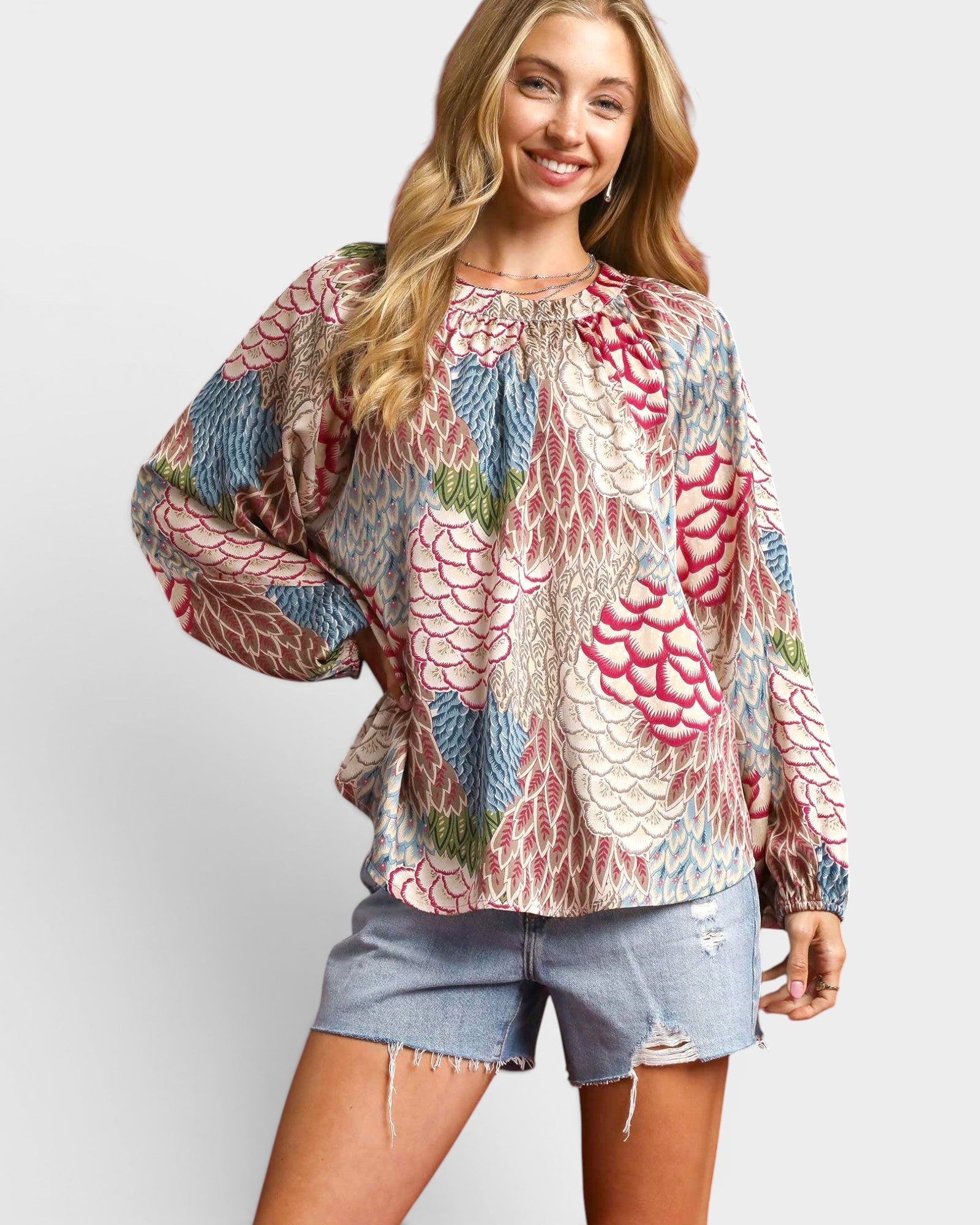 Woman wearing a colorful patterned blouse and denim shorts on a white background