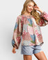 Woman wearing a colorful floral blouse and denim shorts on a white background