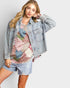 Woman wearing a denim jacket over a patterned shirt with a plain background