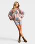 Woman wearing a colorful patterned sweater and denim shorts on a light gray background