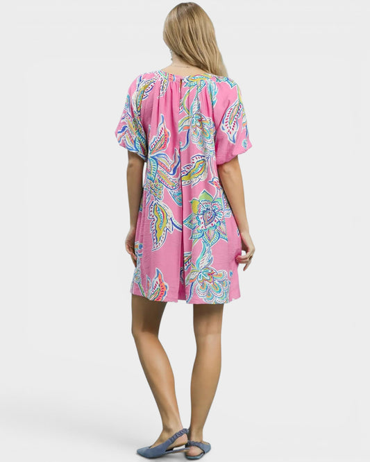 Woman wearing a pink dress with colorful patterns on a white background