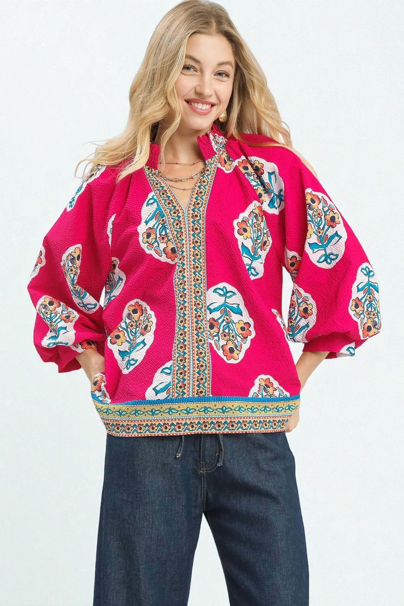 Woman wearing a bright pink blouse with colorful patterns on a white background