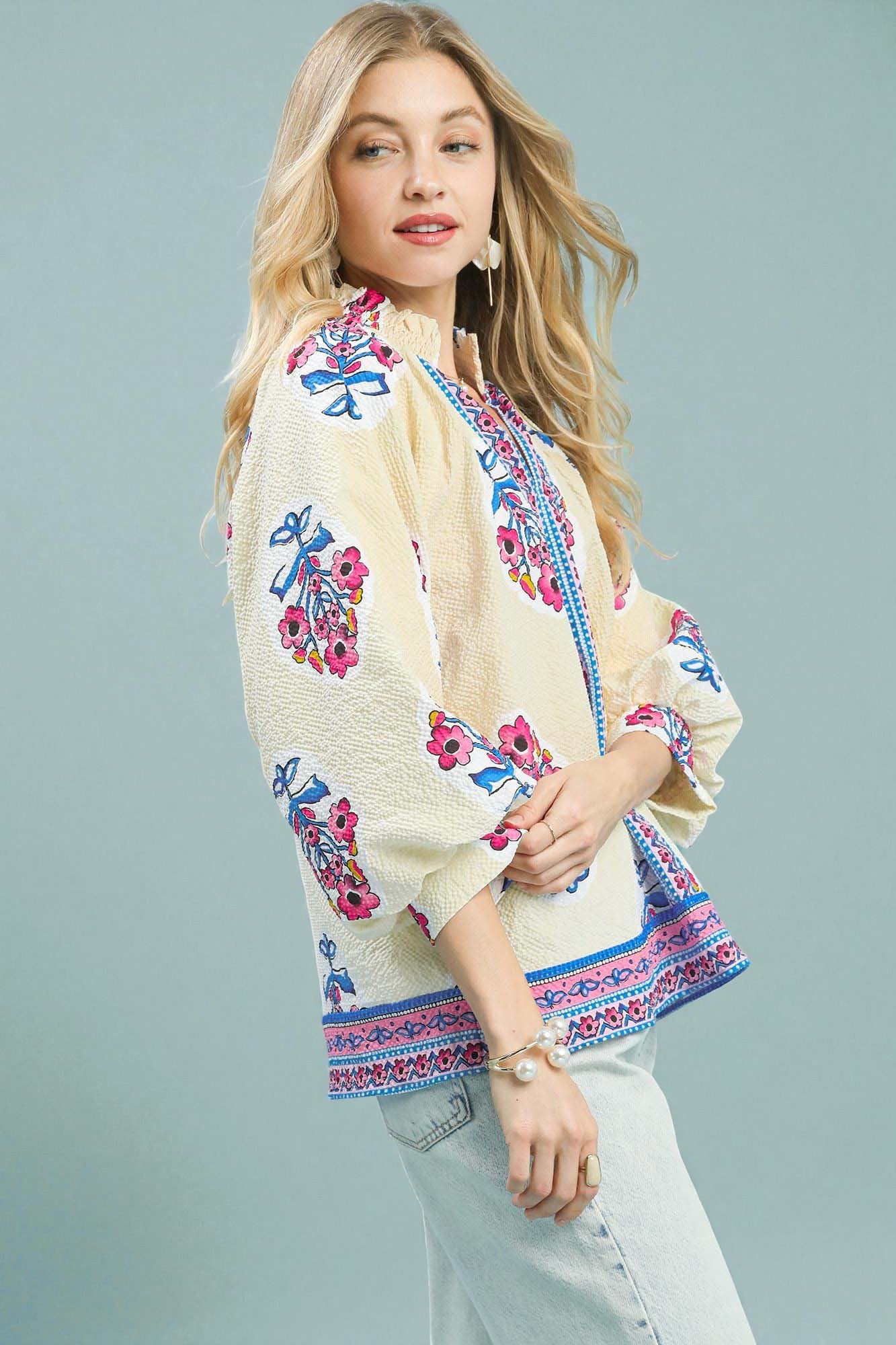 Woman wearing a colorful embroidered top against a light blue background