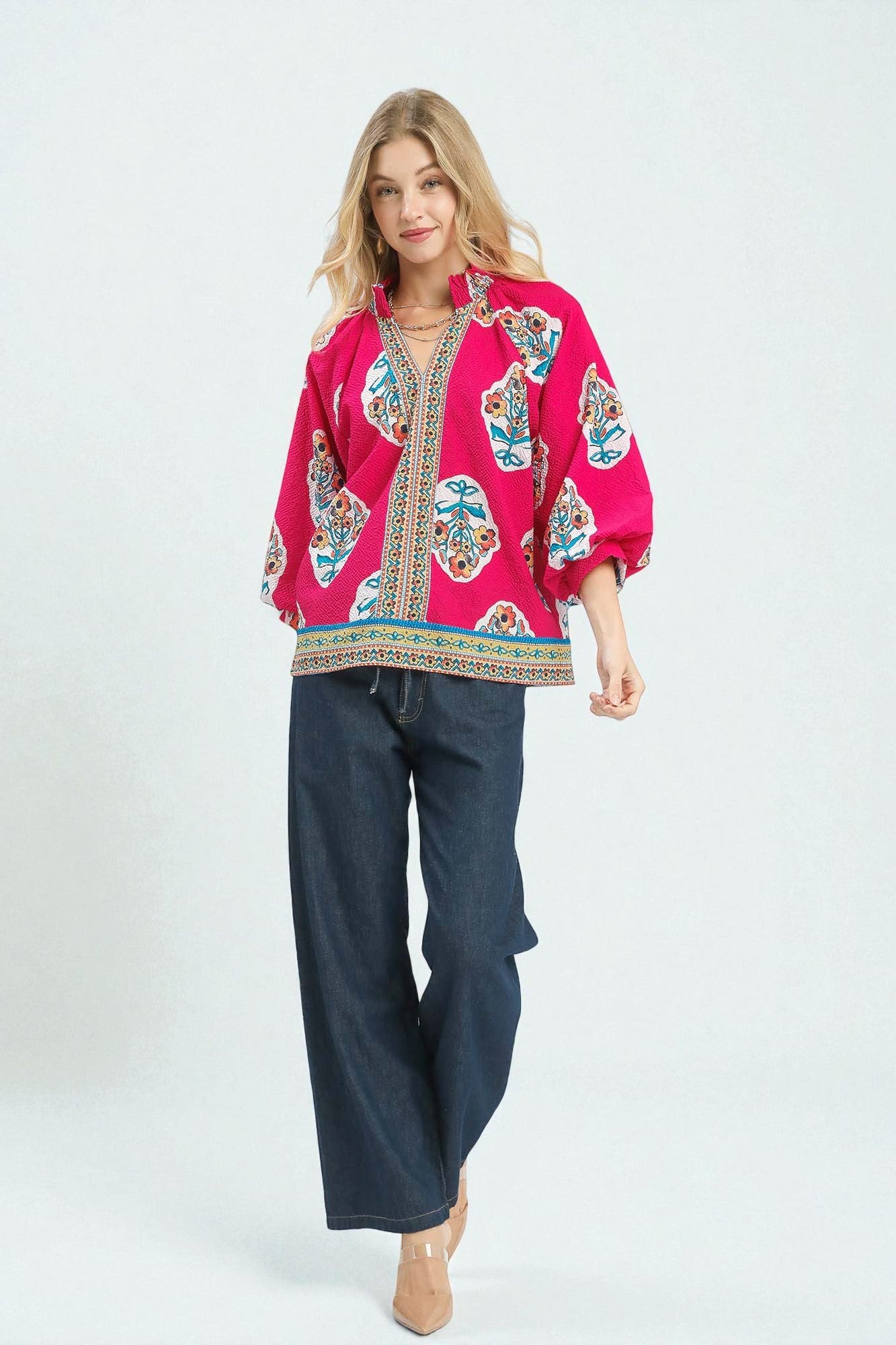 Woman wearing a bright pink embroidered blouse with blue pants on a white background