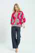 Woman wearing a bright pink embroidered blouse with blue pants on a white background