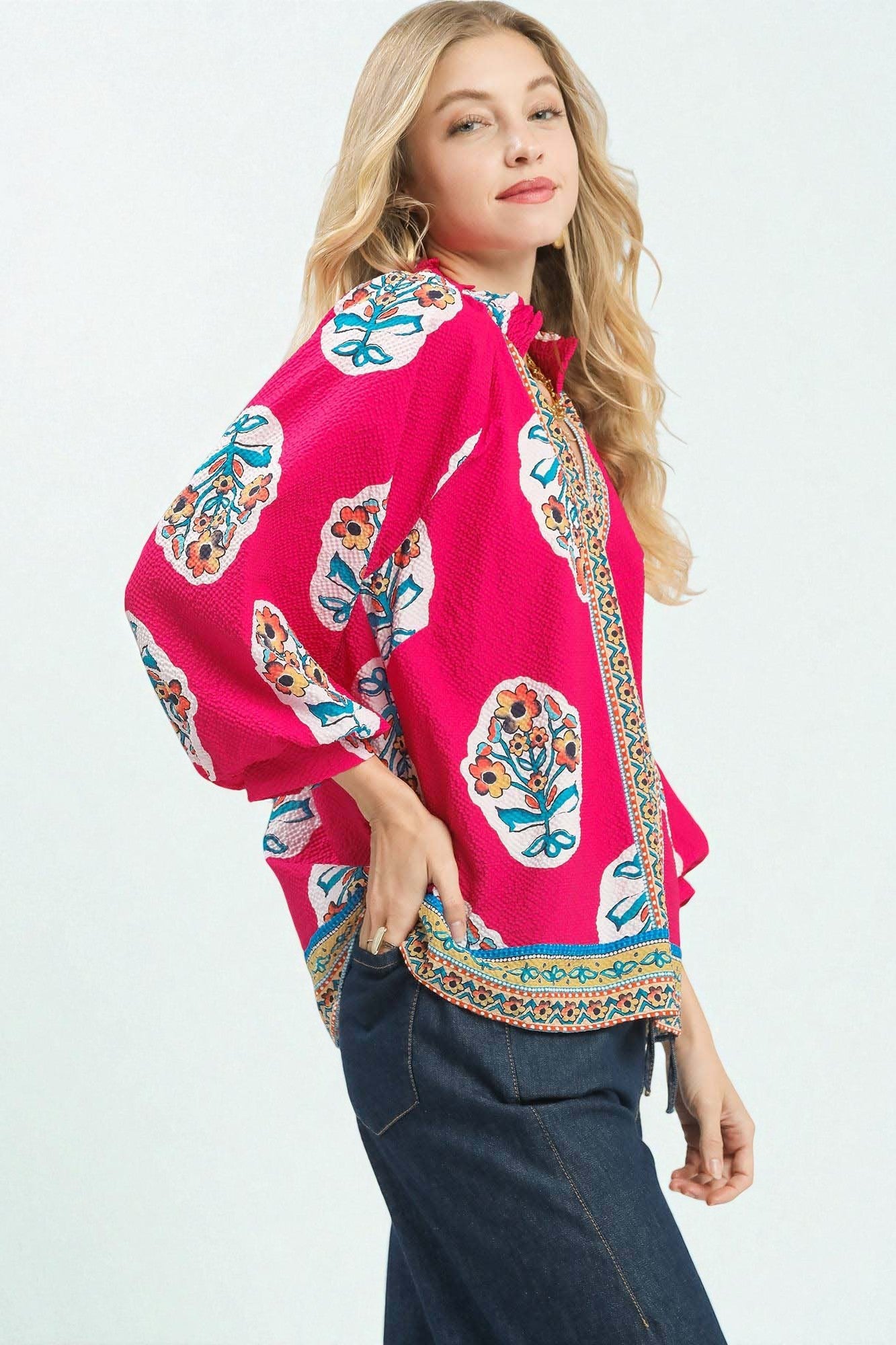 Woman wearing a bright pink blouse with colorful floral patterns on a white background
