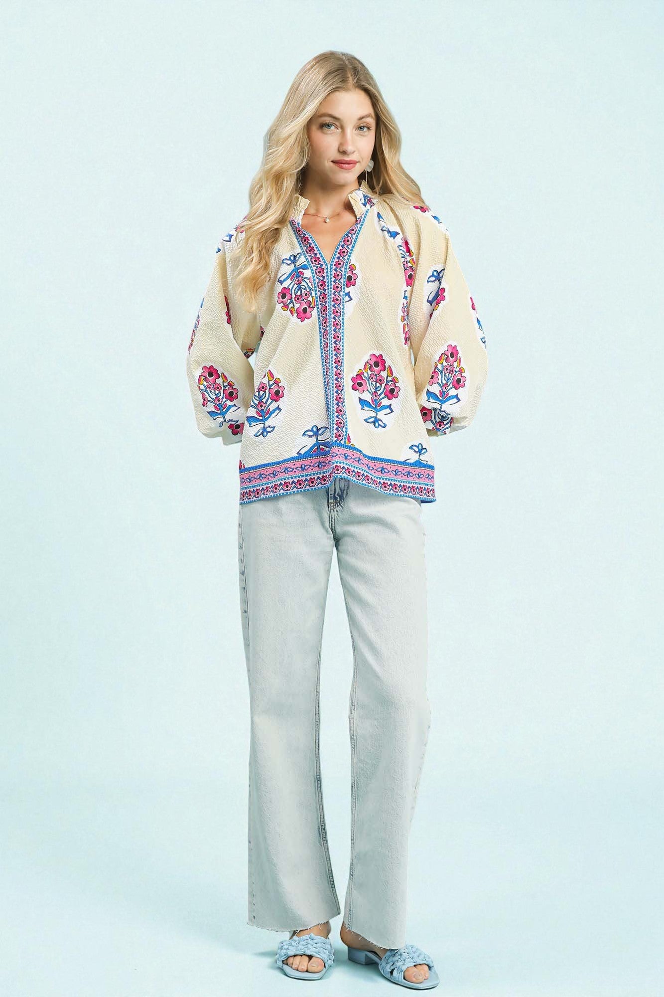 Woman wearing a colorful embroidered blouse and light pants on a light blue background