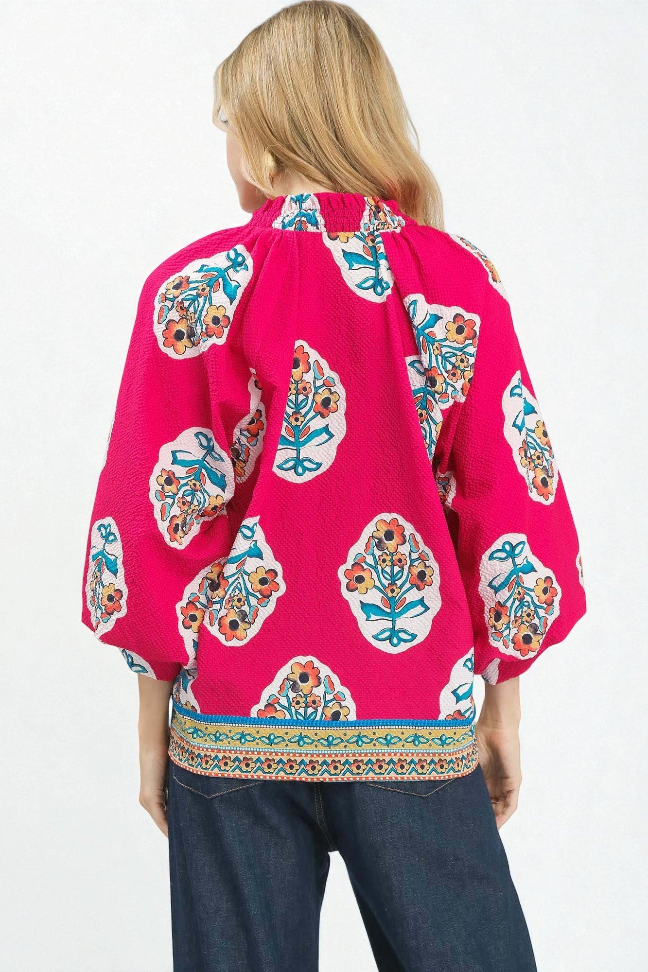 Woman wearing a bright pink blouse with colorful floral patterns on a white background