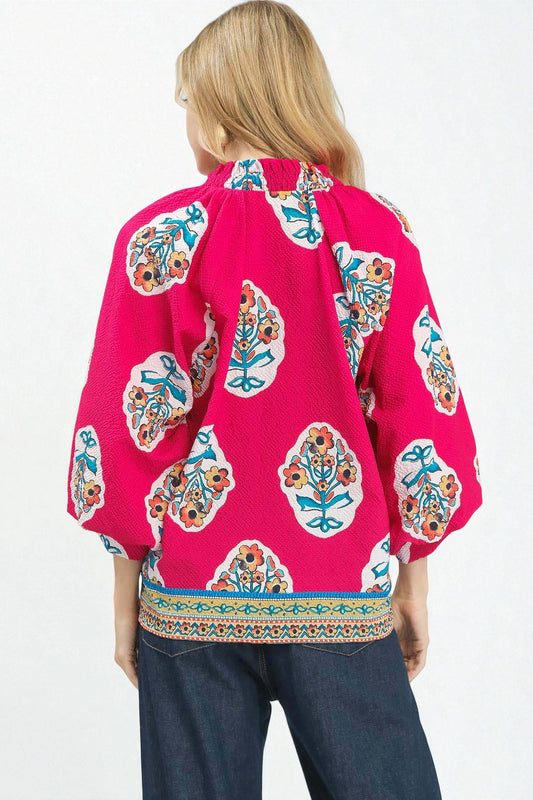 Woman wearing a bright pink blouse with colorful floral patterns on a white background