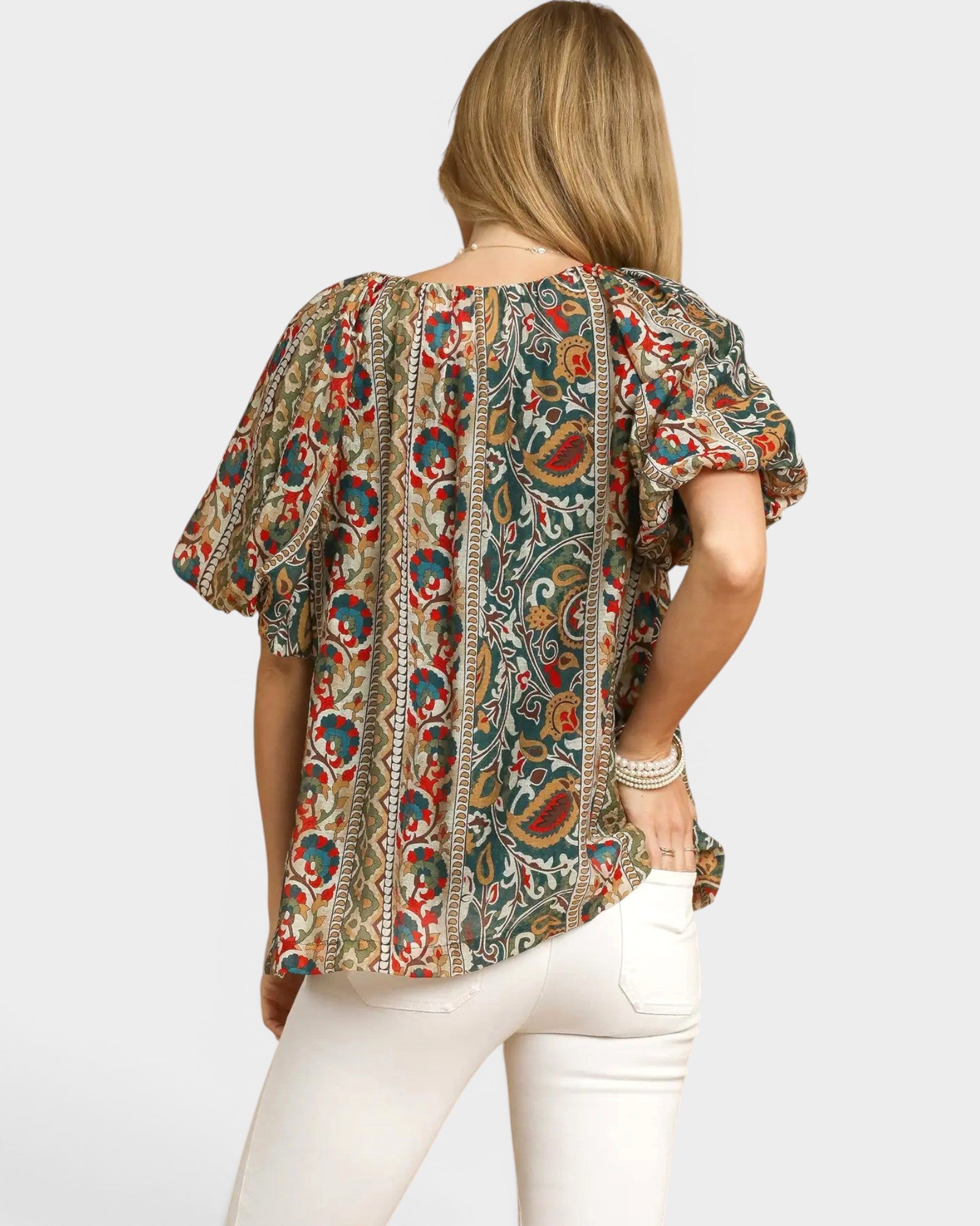 Woman wearing a colorful patterned blouse and white pants on a light gray background
