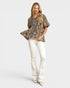 Woman wearing a patterned blouse and white pants on a plain background