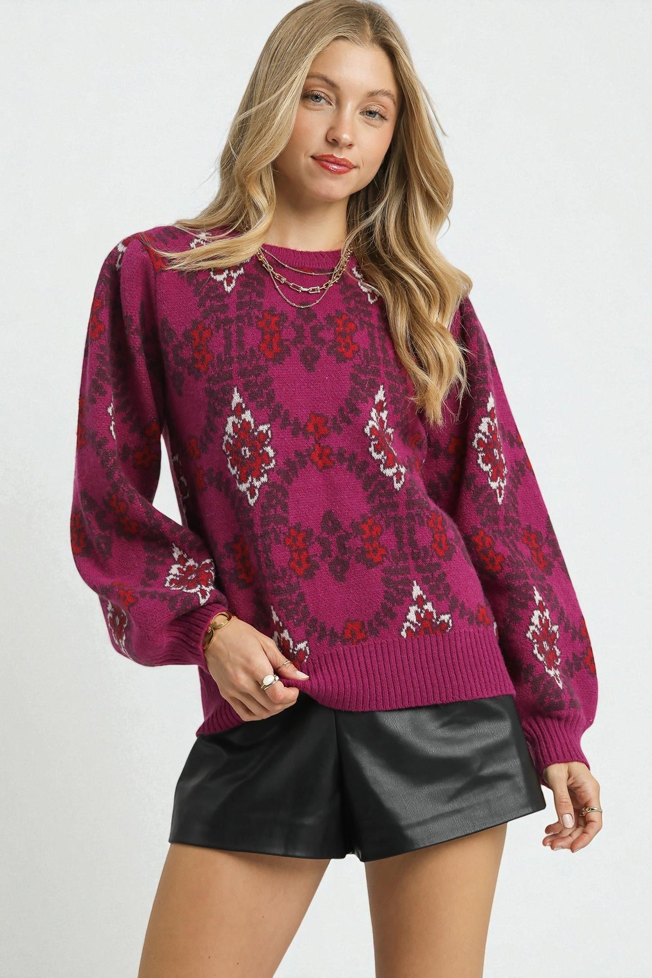 Woman wearing a patterned magenta sweater and black leather shorts on a white background