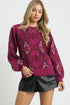 Woman wearing a patterned magenta sweater and black leather shorts on a white background