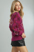 Woman wearing a patterned pink sweater and black leather skirt on a gray background