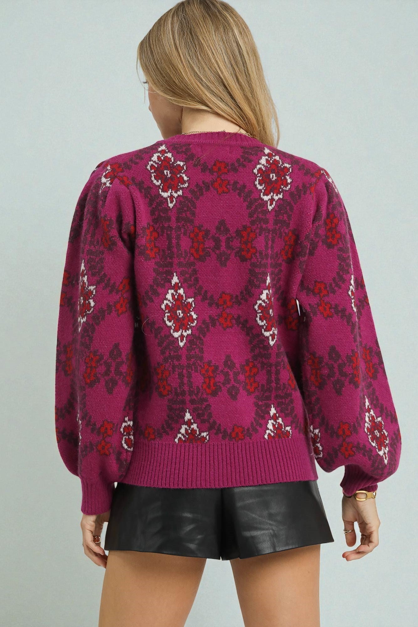 Person wearing a pink patterned sweater and black shorts on a plain background