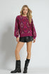 Woman wearing a patterned purple sweater, black leather shorts, and black boots on a white background