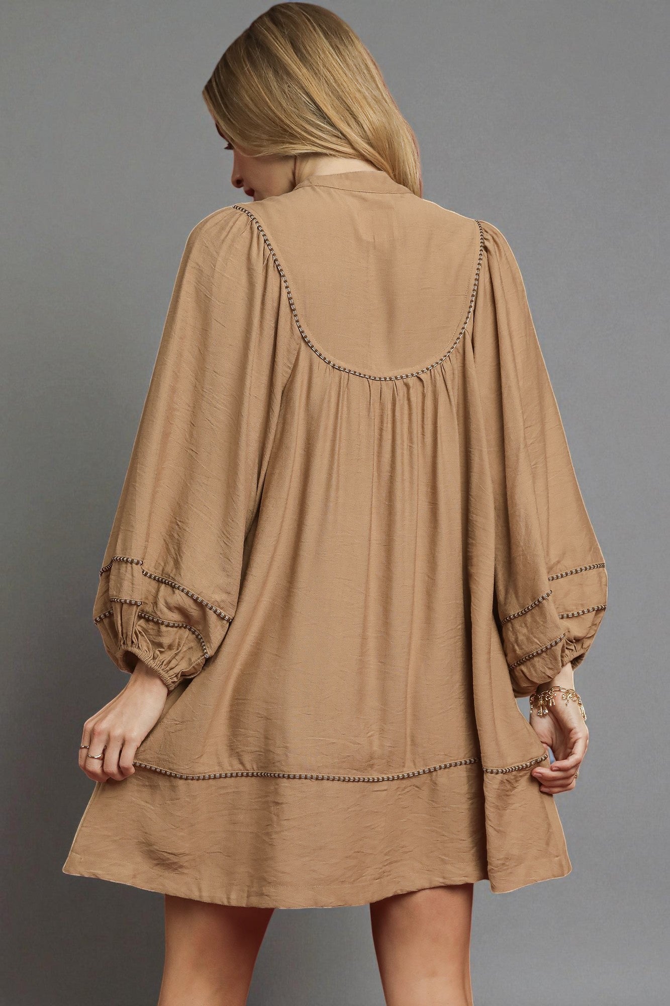 Woman wearing a brown dress with intricate detailing on a gray background