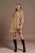 Woman wearing a beige dress and black boots against a brown background
