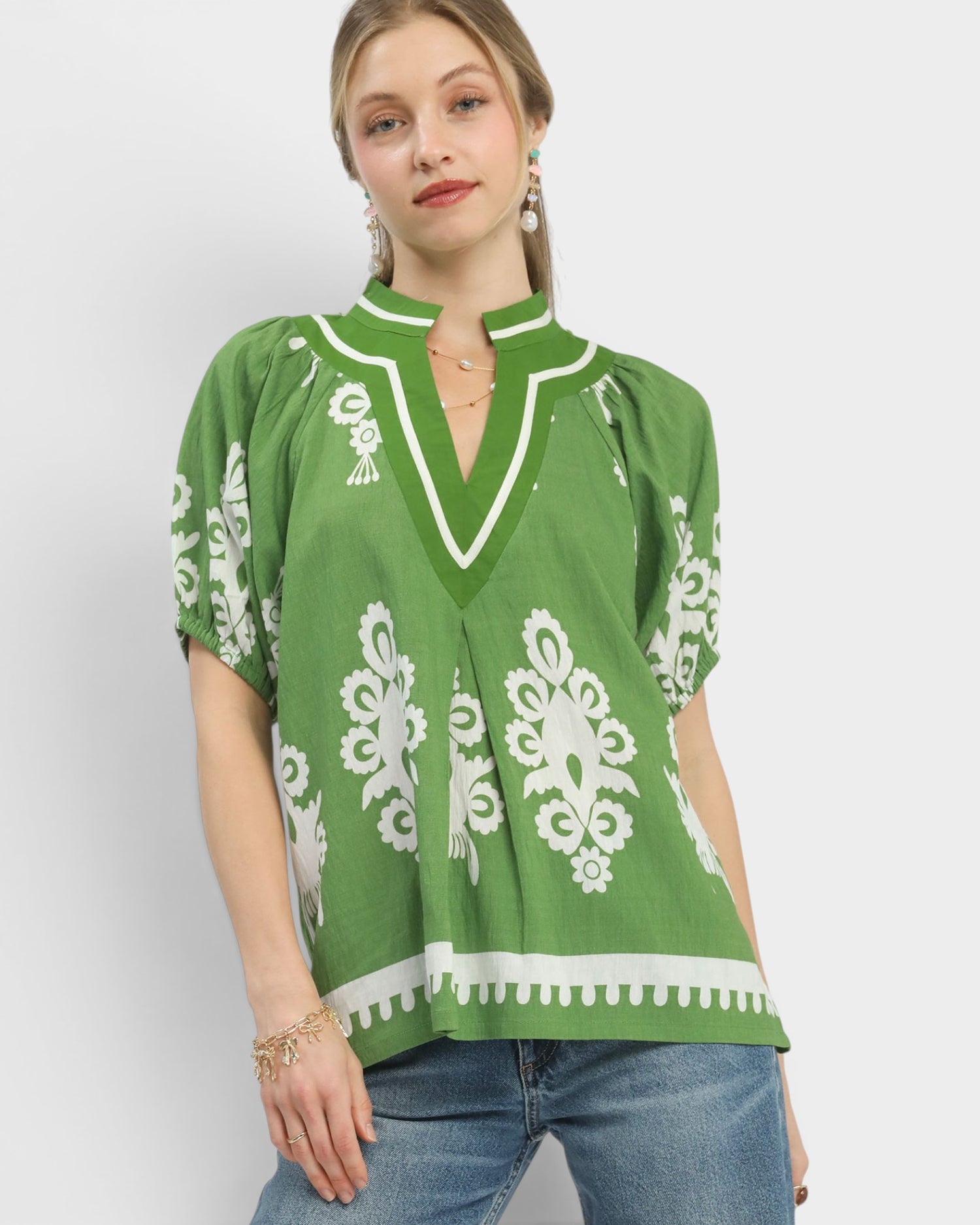 Woman wearing a green blouse with white patterns on a plain background