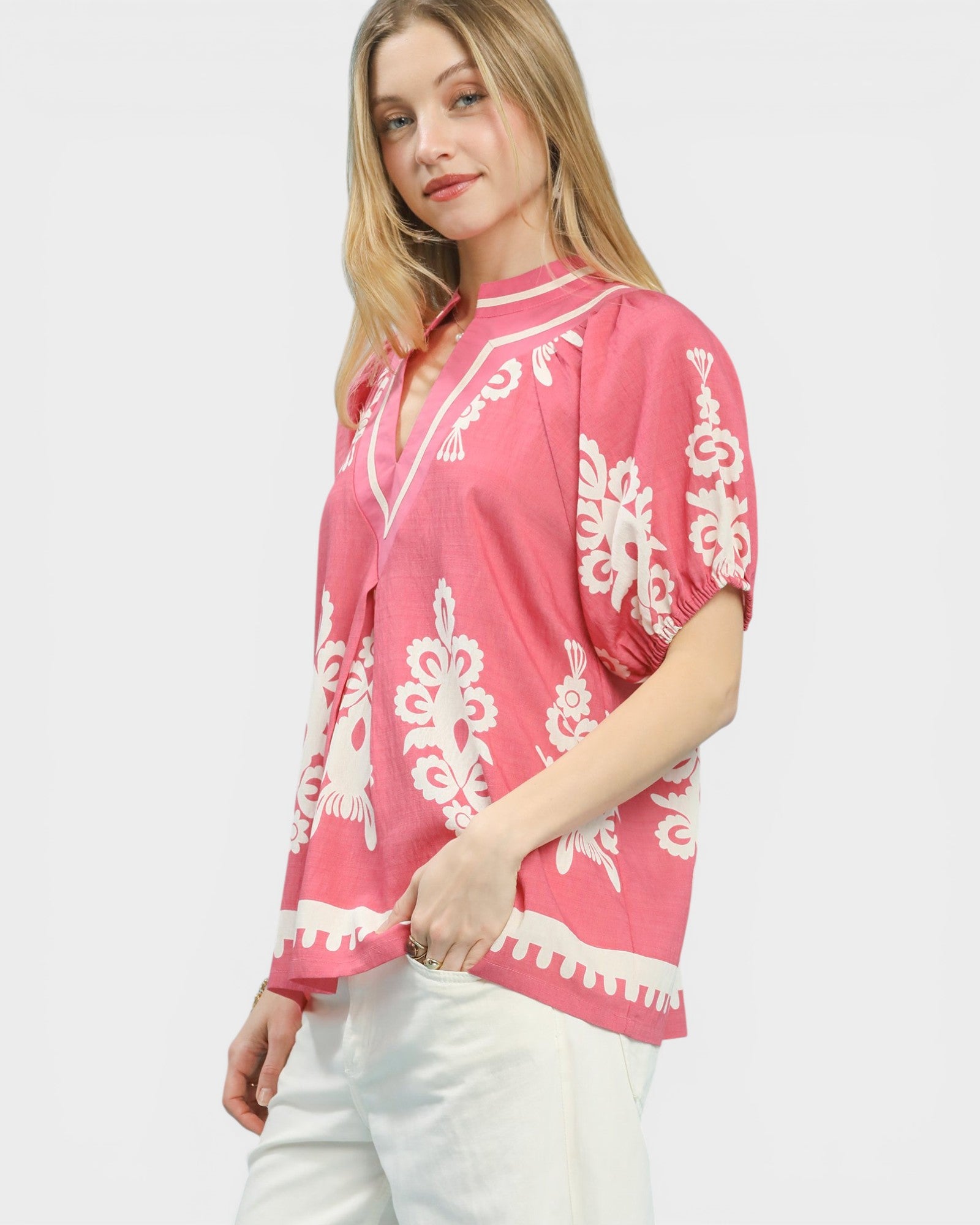 Woman wearing a pink blouse with white patterns on a white background