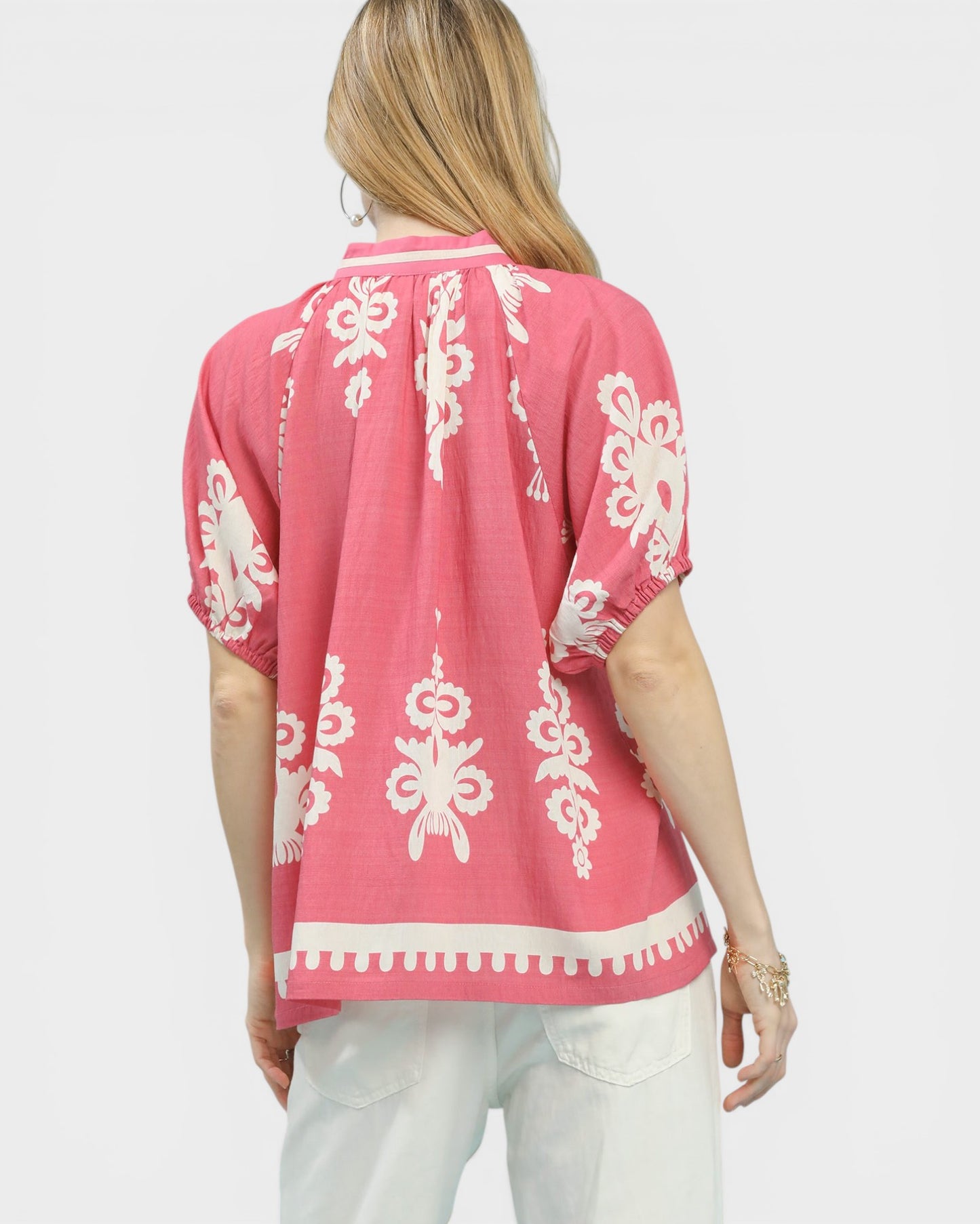 Woman wearing a pink top with white patterns on a plain background