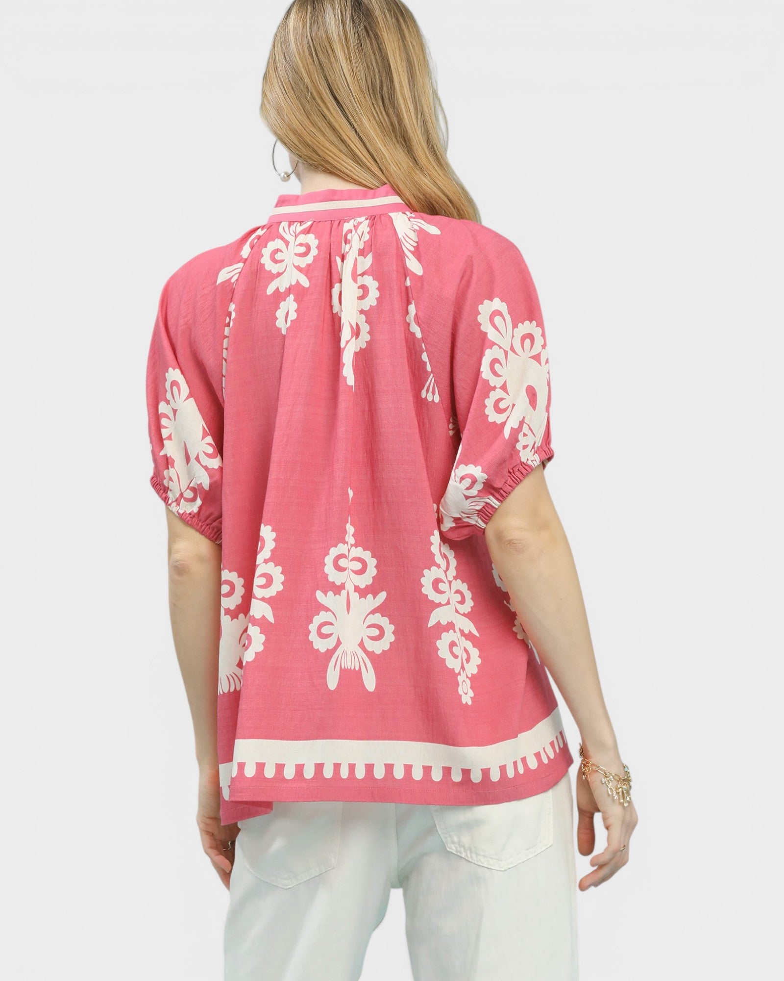 Woman wearing a pink top with white patterns on a plain background