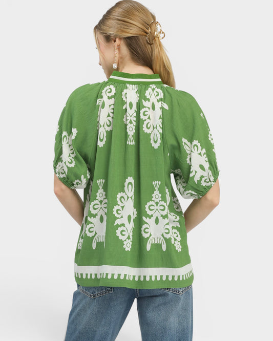 Green top with white lace patterns worn by a person on a white background