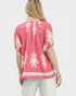 Woman wearing a pink top with white patterns on a plain background