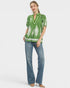 Woman wearing a green blouse with white patterns and blue jeans on a white background