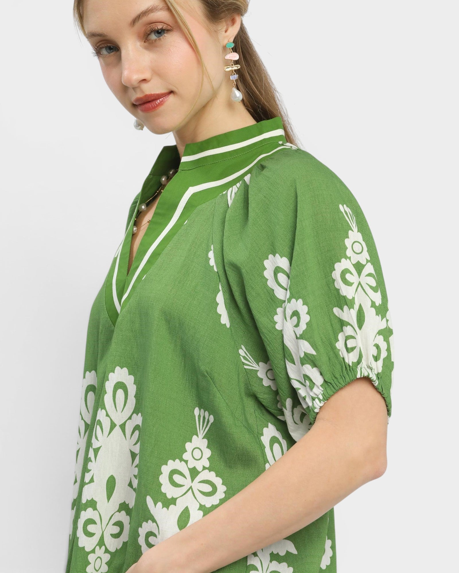 Woman wearing a green blouse with white floral patterns on a plain background