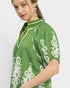Woman wearing a green blouse with white floral patterns on a plain background