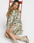 Woman sitting on a red chair wearing a patterned dress and beige boots.