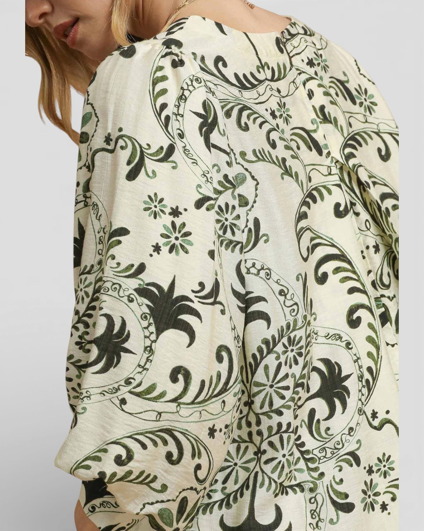 Close-up of a person wearing a patterned top with green and black designs on a plain background