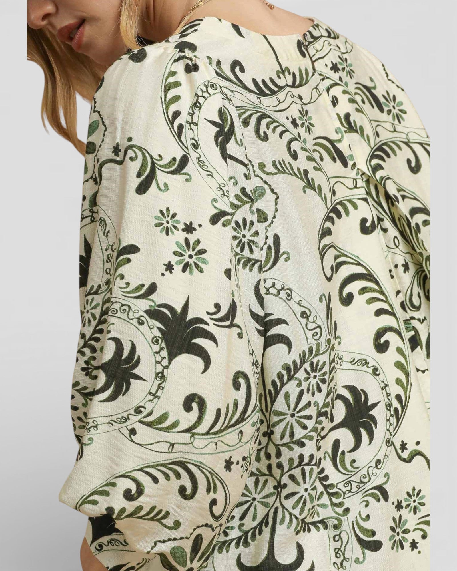 Close-up of a person wearing a patterned top with green and black designs on a plain background